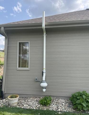 Radonsystem installerat på en beige husvägg med tak och fönster.