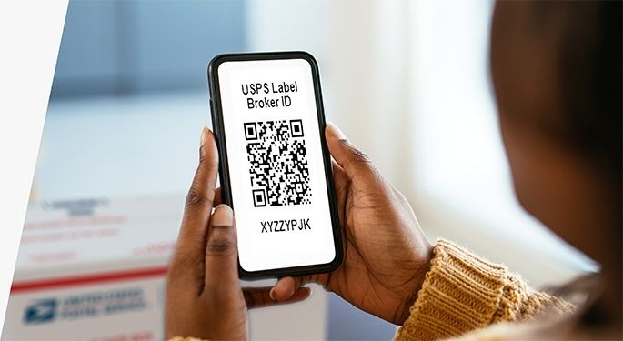 Person håller upp en mobil med QR-kod för en fraktetikett